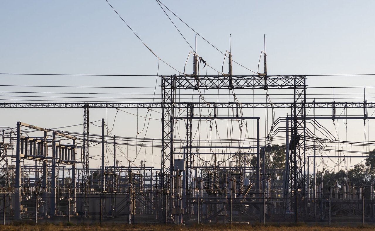 Subestação elétrica com estruturas metálicas e linhas de alta tensão ao amanhecer.