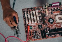 Profissional utilizando uma ferramenta de solda em uma placa-mãe durante trabalho de desenvolvimento de hardware.