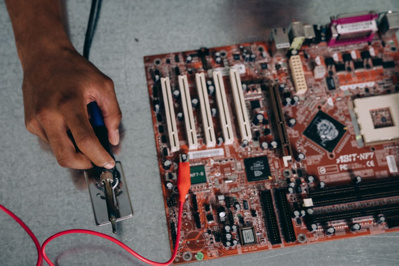 Profissional utilizando uma ferramenta de solda em uma placa-mãe durante trabalho de desenvolvimento de hardware.