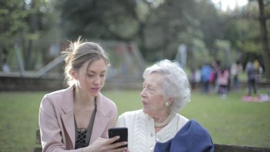 Mulher orienta uma idosa no uso do celular enquanto estão sentadas em um banco de parque.