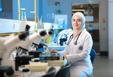 Cientista realiza pesquisa em laboratório diante de um microscópio e livros de referência.