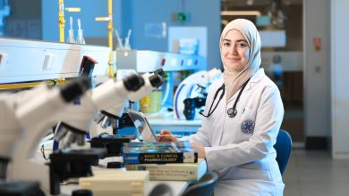 Cientista realiza pesquisa em laboratório diante de um microscópio e livros de referência.