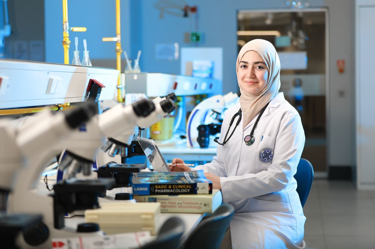 Cientista realiza pesquisa em laboratório diante de um microscópio e livros de referência.
