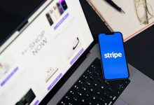 Smartphone exibindo um aplicativo de pagamentos diante de um laptop com um site de comércio eletrônico aberto.