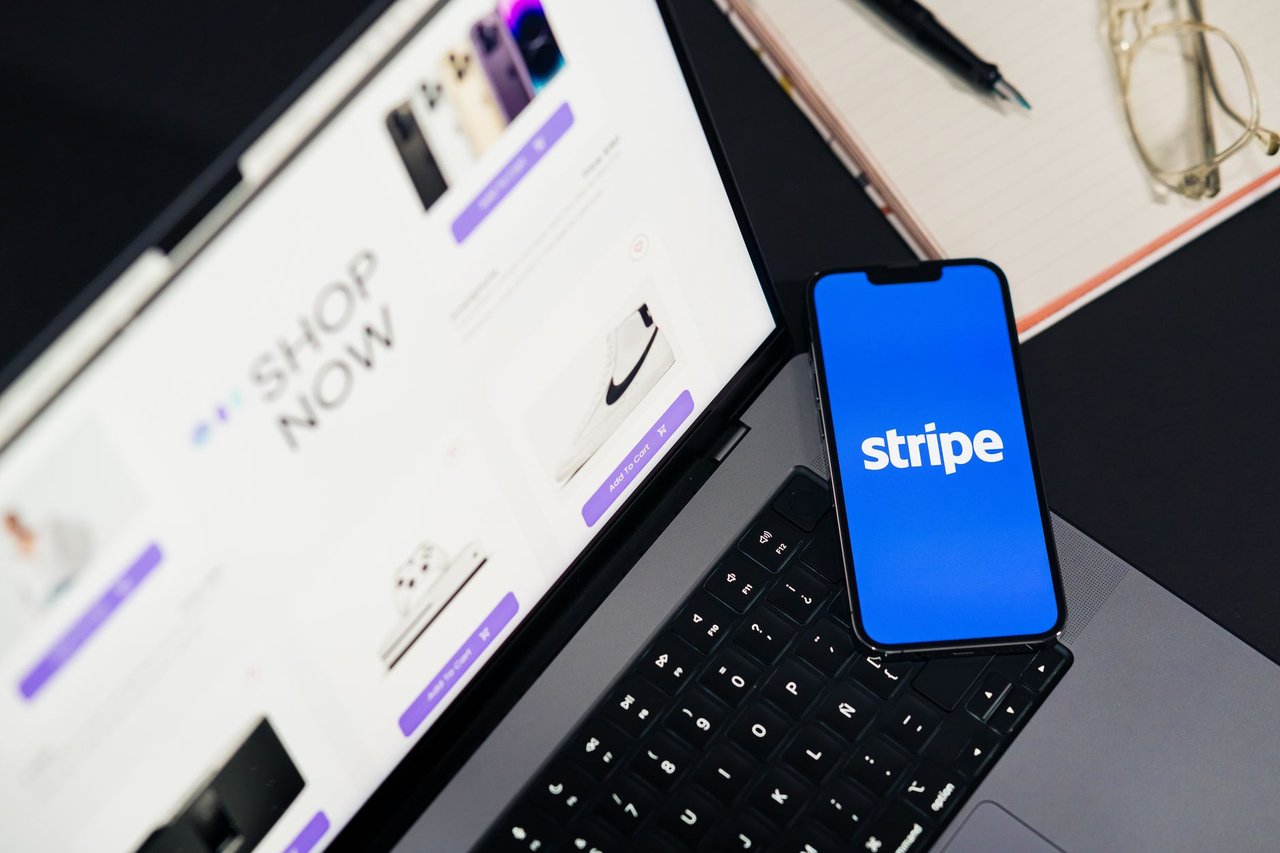 Smartphone exibindo um aplicativo de pagamentos diante de um laptop com um site de comércio eletrônico aberto.