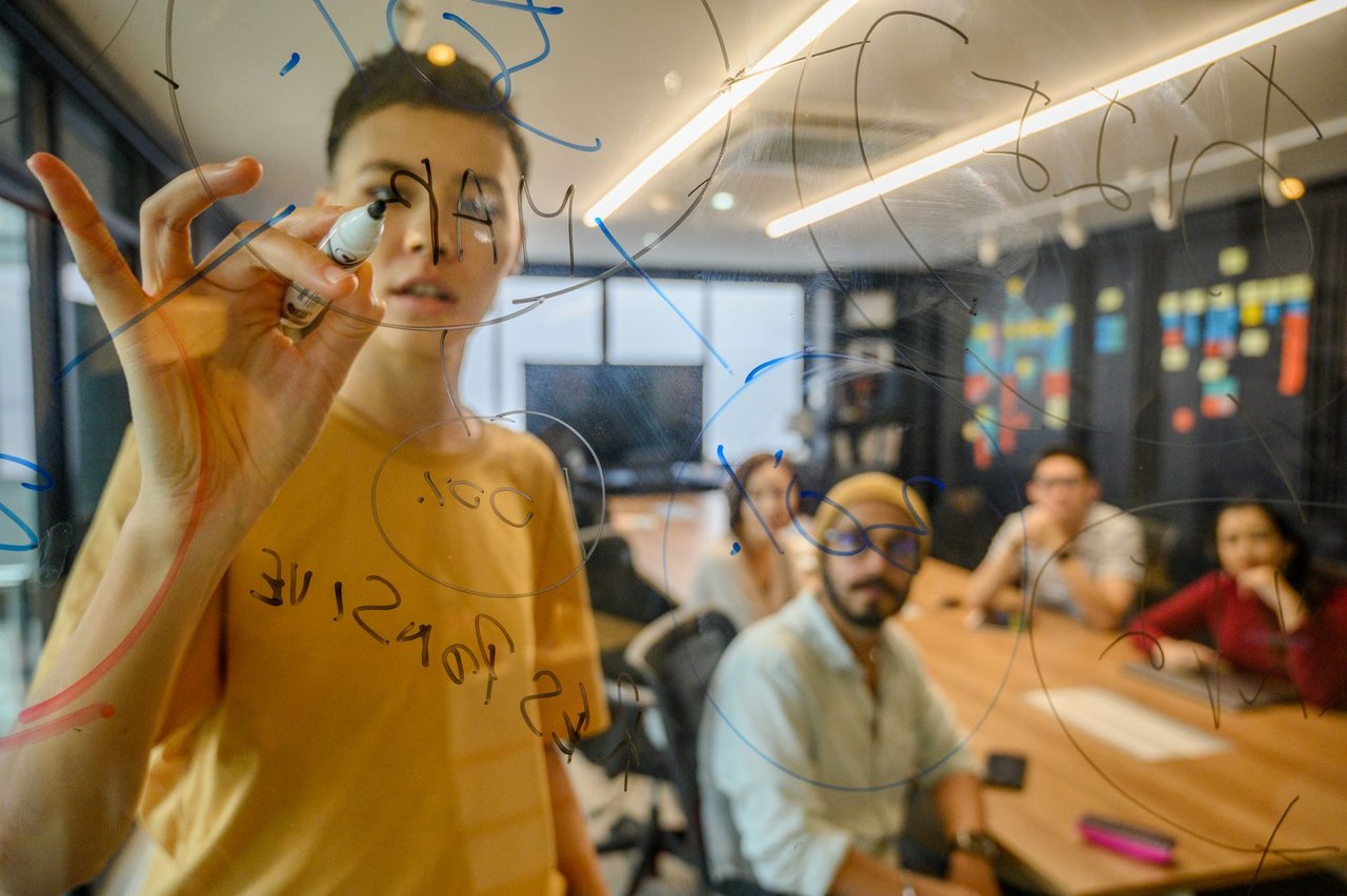Equipe reunida em um escritório moderno, colaborando diante de um quadro de vidro com anotações.