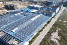 Vista aérea de painéis solares instalados sobre um complexo industrial.